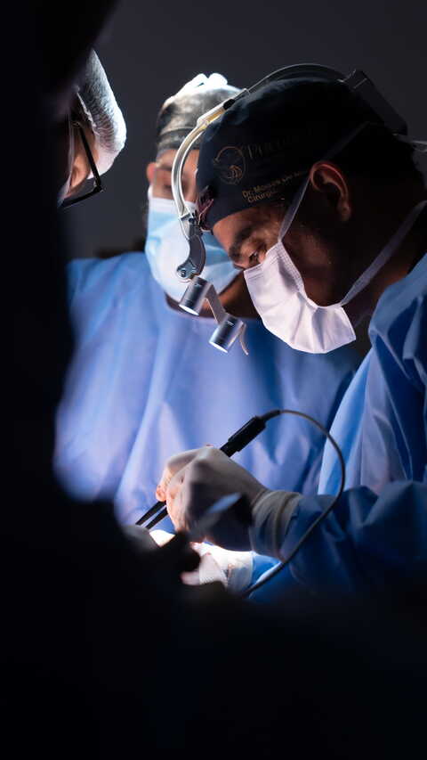 Dr. Moises De Melo realizando procedimento em centro cirúrgico com equipe médica.